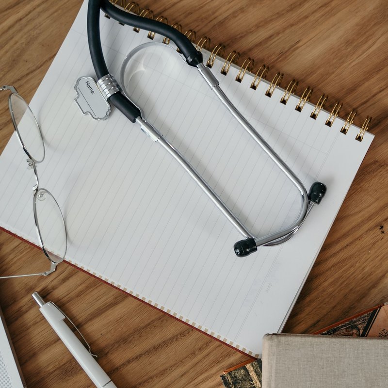 Stethoscope resting across a blank notebook on a wood desk