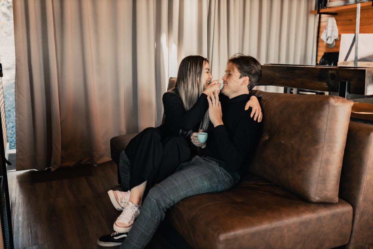 Laughing couple sharing a cup on a brown leather sofa