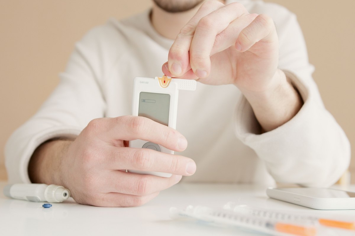 Hands holding a white glucose meter and test strip at a table