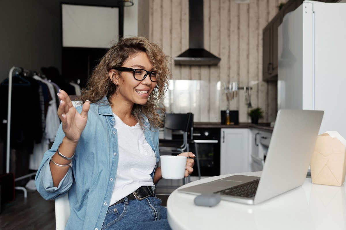 Smiling woman with glasses talking over a laptop at her kitchen table