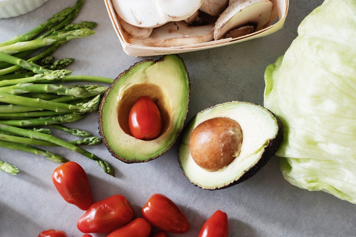 Avocado halves and fresh vegetables arranged on a tabletop