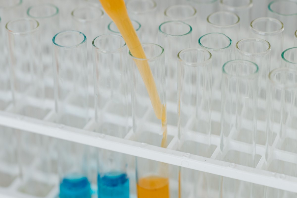 Pipette transferring orange liquid into a glass test tube in a laboratory