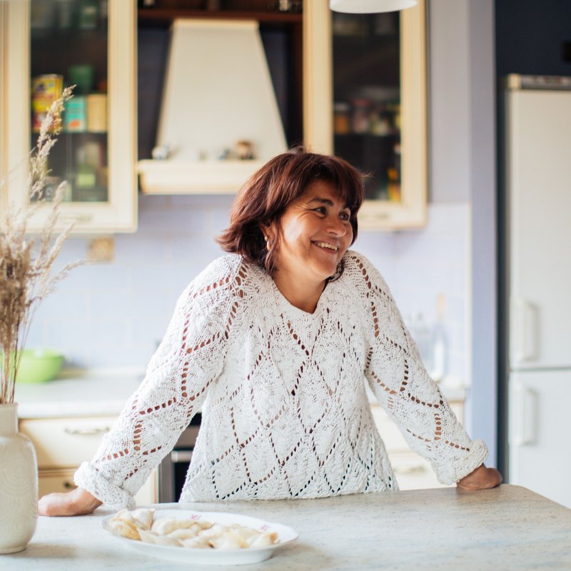 Smiling woman in a white knit sweater leaning on a kitchen counter at home
