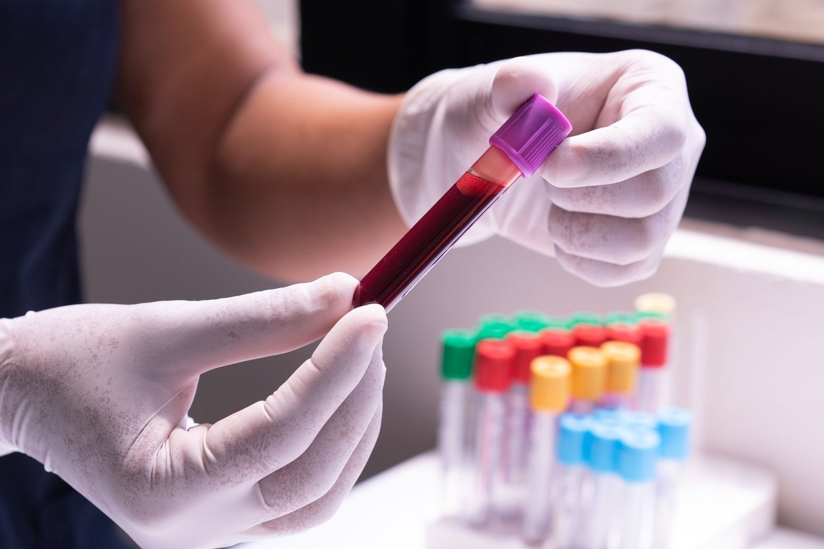 White-gloved hands examining a purple-capped blood sample tube