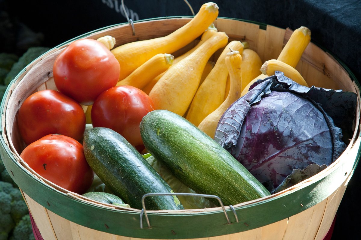 Wooden basket holding tomatoes, squash, zucchini and a purple cabbage
