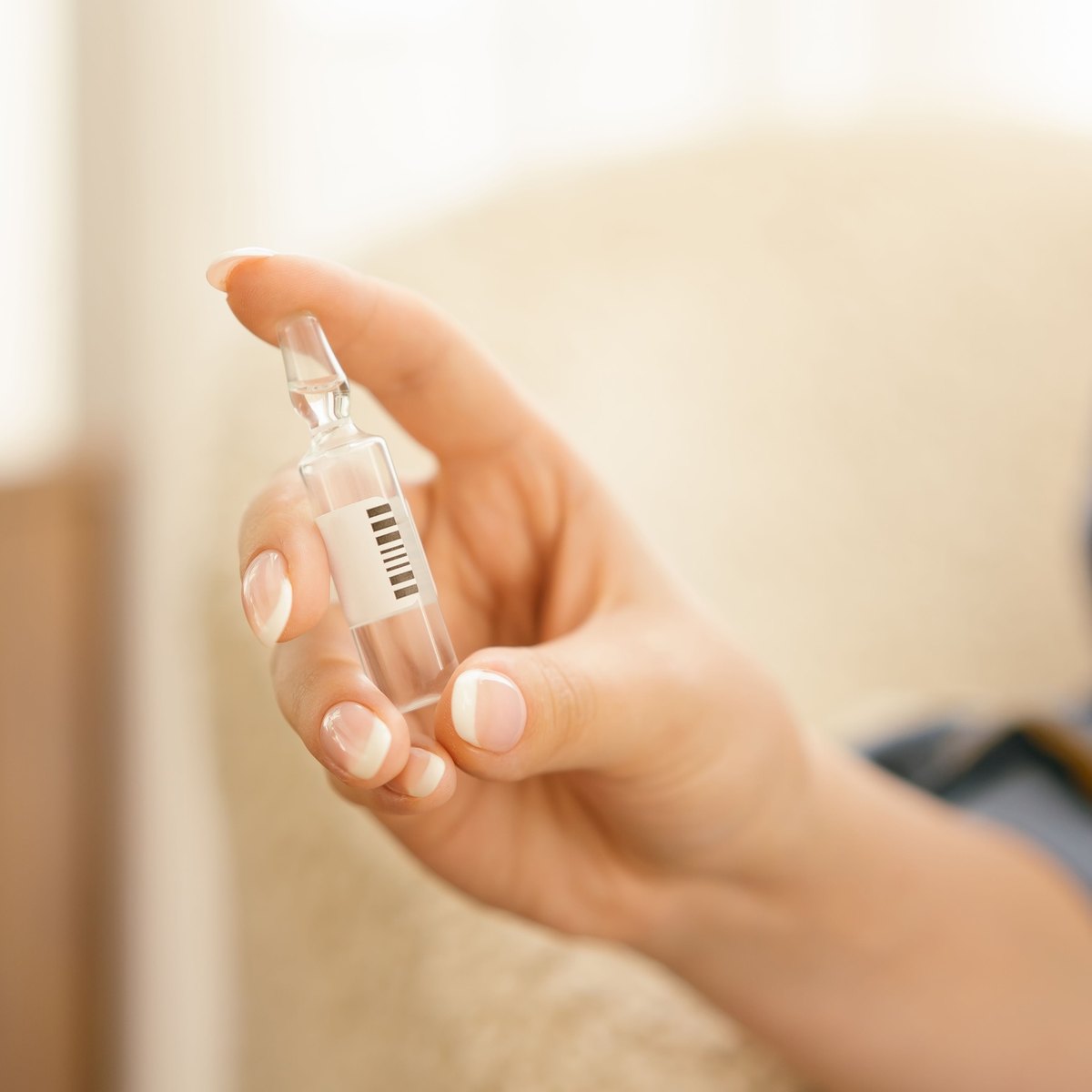 Hand holding a small clear glass ampoule with a plain barcode label