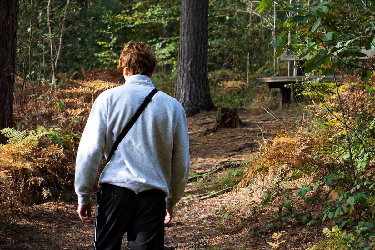 Man in a pale blue fleece walking along a wooded trail